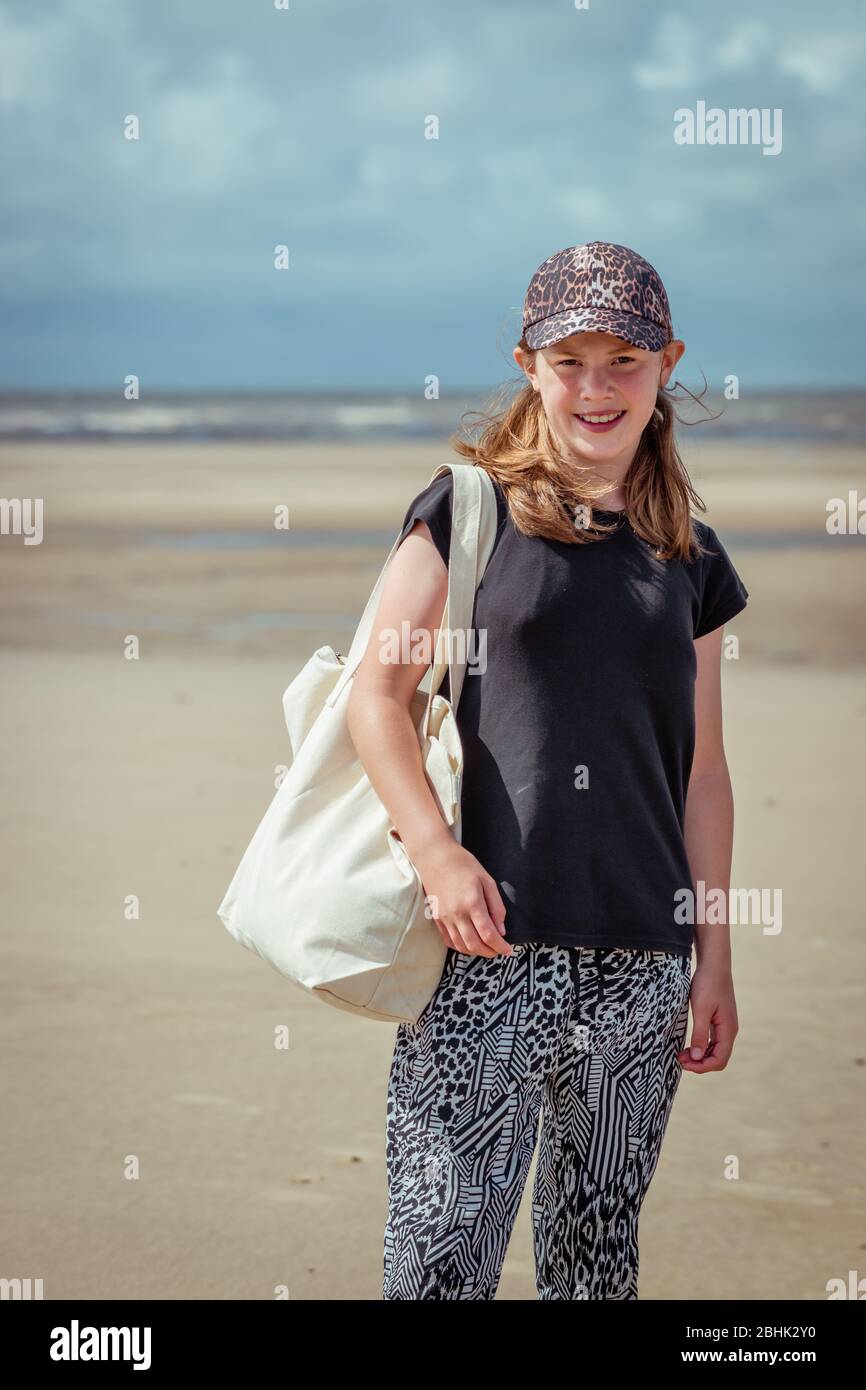 Une adolescente se tenant sur une plage avec sac fourre-tout à la crème et casquette Banque D'Images