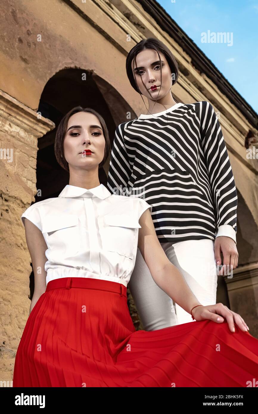 Piscine fashion portrait de deux jeunes et belles femmes portant des vêtements à la mode qui posent sur la rue dans le contexte d'un vieux abandonné buil Banque D'Images