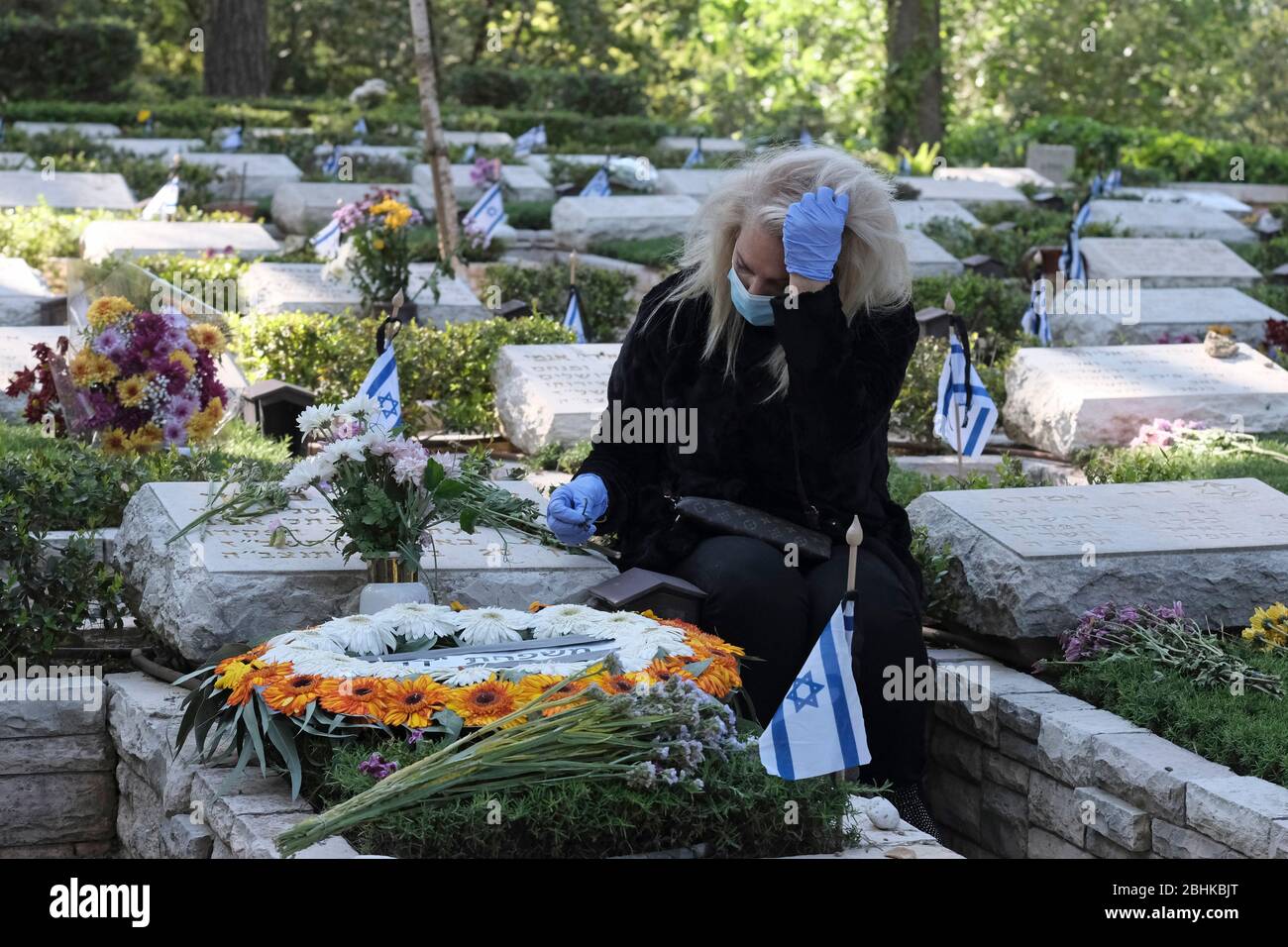 Jérusalem, Israël. 26 avril 2020. Une israélienne portant un masque protecteur en raison de la pandémie du coronavirus COVID-19 grit sur la tombe d'un être cher dans l'armée nationale du Mont-Herzl à Jérusalem alors qu'Israël se prépare à marquer le jour du souvenir des soldats tombés. Les cérémonies officielles ne se dérouleront pas cette année en raison d'un couvre-feu national pour lutter contre la pandémie COVID-19. Banque D'Images
