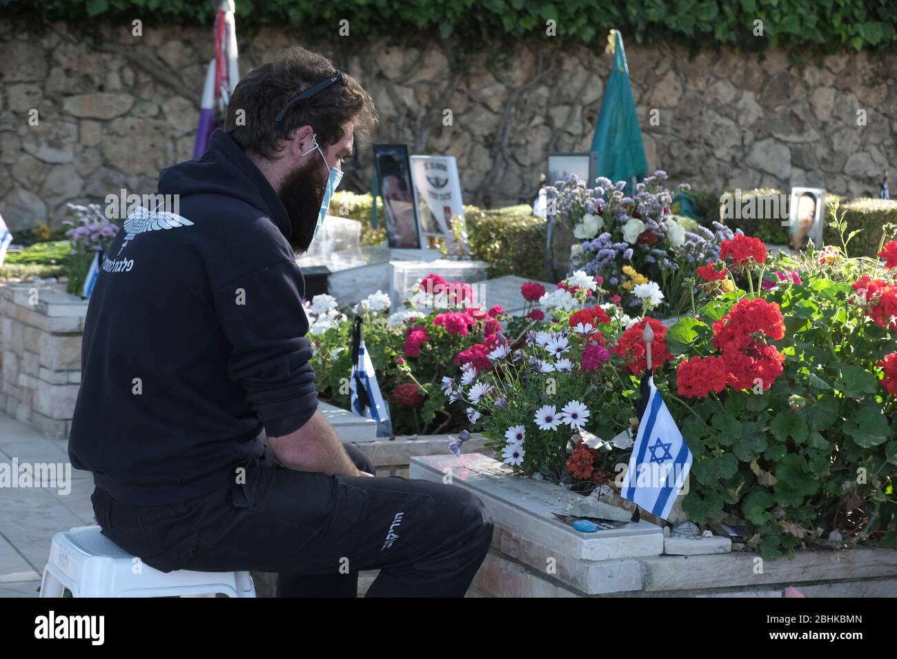 Jérusalem, Israël. 26 avril 2020. Un jeune israélien portant un masque protecteur en raison de la pandémie du coronavirus COVID-19 respecte la tombe d'un être cher de l'armée nationale du Mont-Herzl à Jérusalem alors qu'Israël se prépare à marquer le jour du souvenir des soldats tombés. Les cérémonies officielles ne se dérouleront pas cette année en raison d'un couvre-feu national pour lutter contre la pandémie COVID-19. Banque D'Images