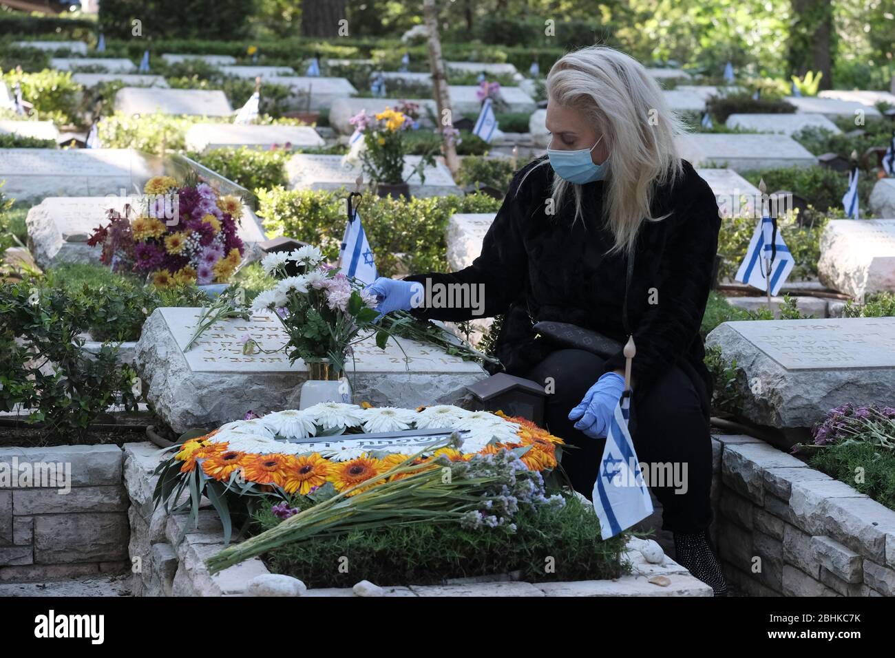 Jérusalem, Israël. 26 avril 2020. Une femme israélienne portant un masque protecteur en raison de la pandémie de coronavirus du COVID-19 se crasse sur la tombe d'un être cher au cimetière militaire du Mont-Herzl à Jérusalem alors qu'Israël se prépare à marquer la journée commémorative des soldats tombés. Les cérémonies officielles n'auront pas lieu cette année en raison d'un couvre-feu national pour lutter contre la pandémie de COVID-19. Banque D'Images