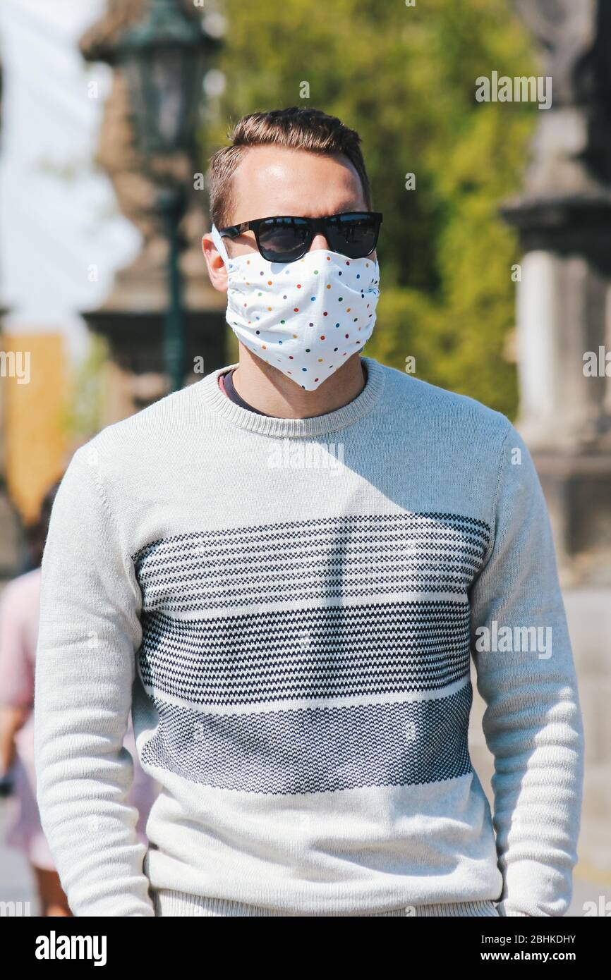 Jeune homme avec lunettes de soleil et masque en tissu cousu photographié sur le pont Charles à Prague, en République tchèque. Arrière-plan flou. Voyager, tourisme pendant coronavirus. COVID-19. Photo verticale. Banque D'Images
