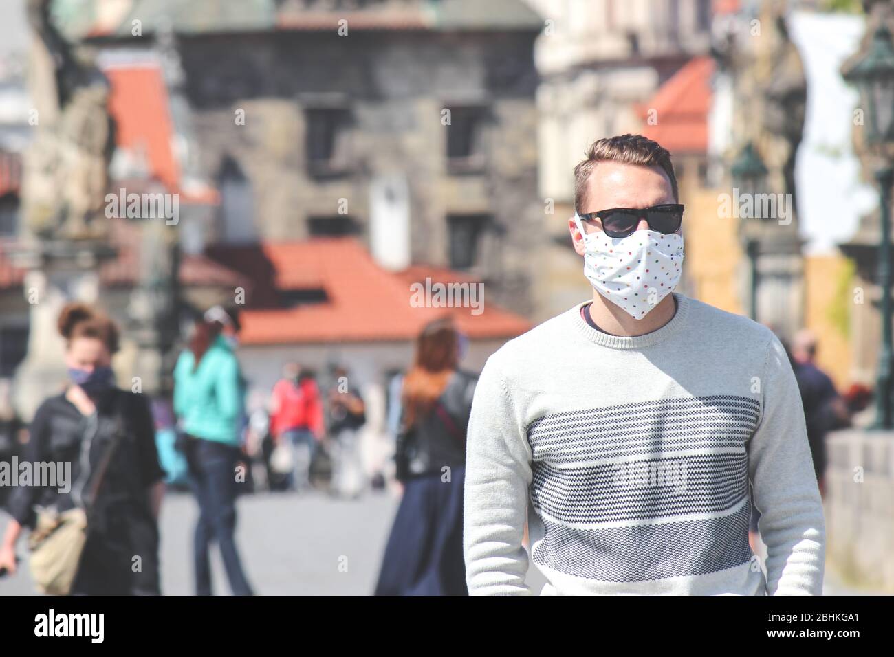 Jeune homme avec lunettes de soleil et masque en tissu cousu photographié sur le pont Charles à Prague, en République tchèque. Brouillé dans l'arrière-plan. Voyager, tourisme pendant coronavirus. COVID-19. Banque D'Images