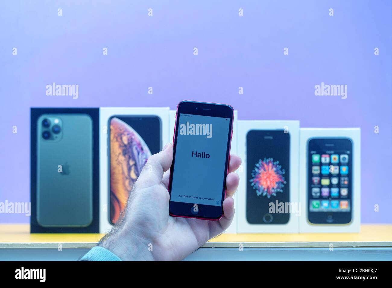 Paris, France - 26 avril 2020: Homme tenant iPhone se avec le mot Hallo avec plusieurs paquets cardboards d'Apple Computers iPhone Smartphpone iPhone 3 gs, se 2016, XS et 11 Pro Banque D'Images