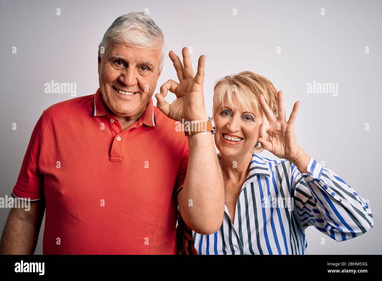 Couple senior magnifique debout ensemble sur un arrière-plan blanc isolé souriant positif faisant signe ok avec la main et les doigts. Expression réussie. Banque D'Images