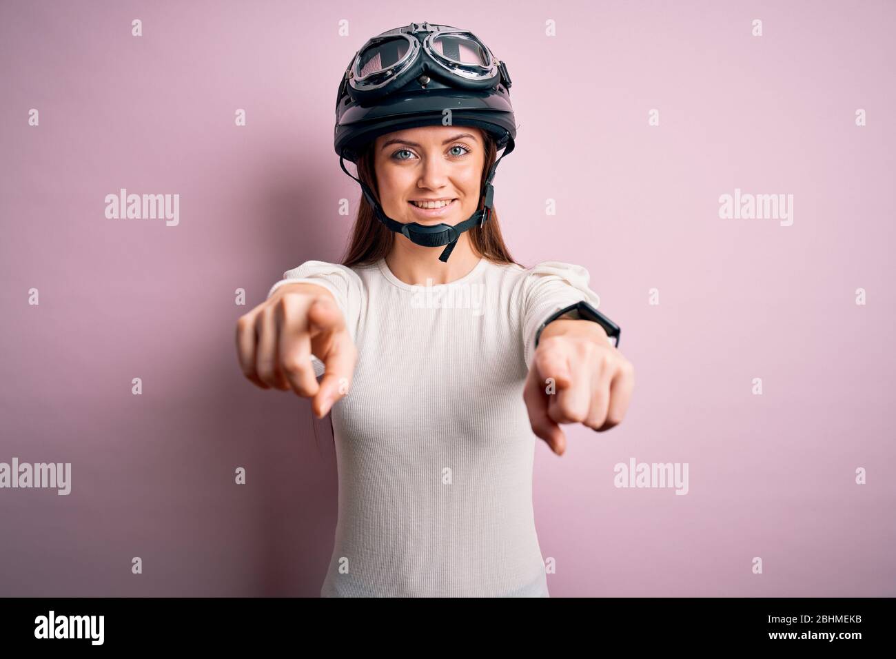 Jeune femme motard et motard, les yeux bleus portent un casque moto sur  fond rose qui vous pointe et l'appareil photo avec les doigts, souriant  positi Photo Stock - Alamy
