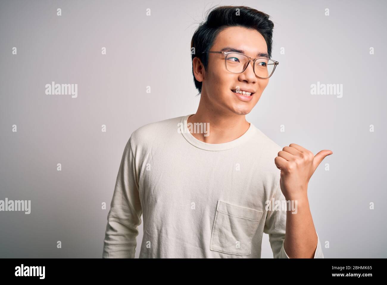 Jeune homme chinois portant un t-shirt décontracté et des lunettes sur fond  blanc souriant avec un visage heureux regardant et pointant sur le côté  avec thum Photo Stock - Alamy