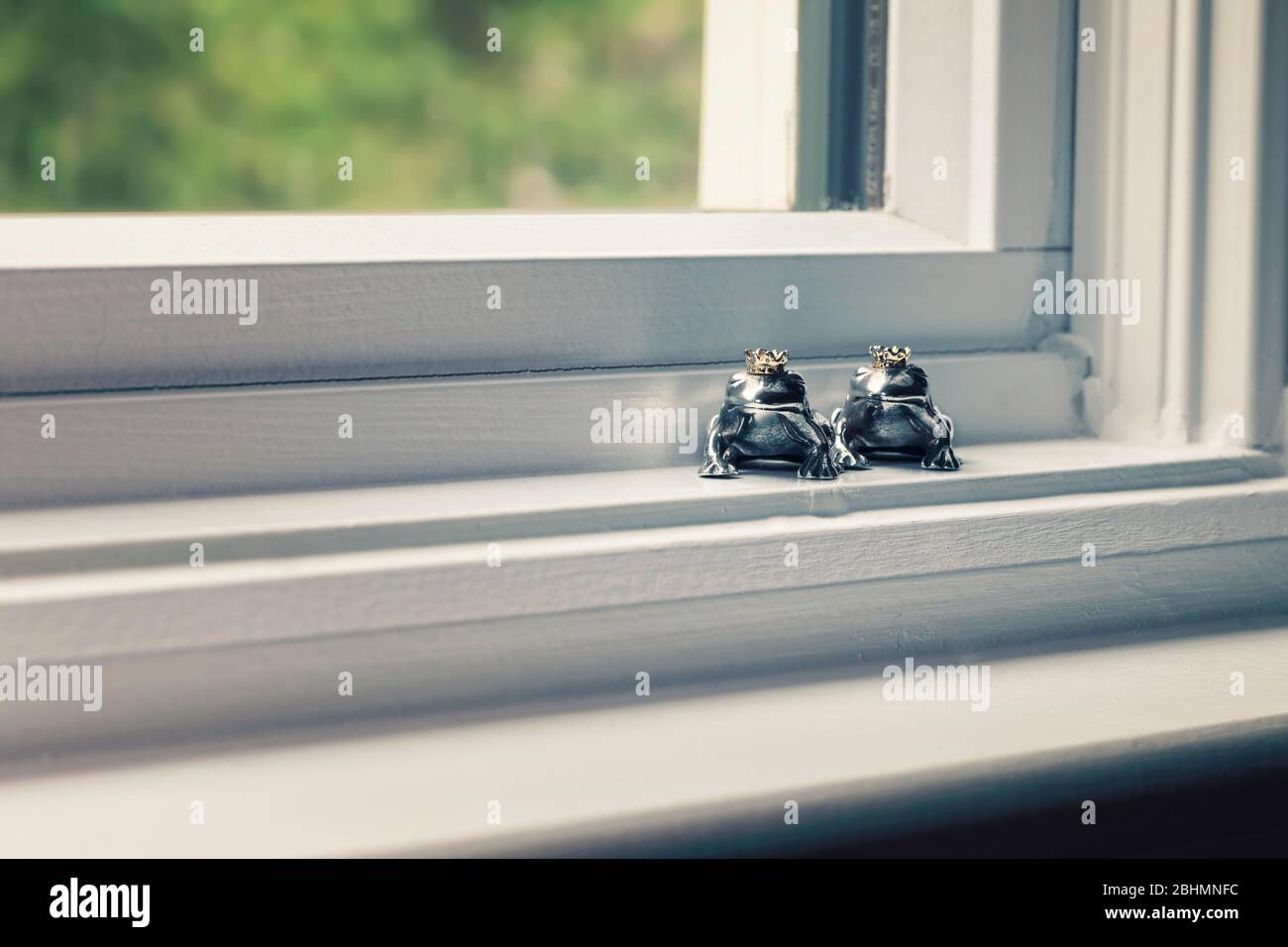 Deux figurines couronnées de prince grenouille en argent sterling assis dans le seuil de vent, concept de couleur. Banque D'Images