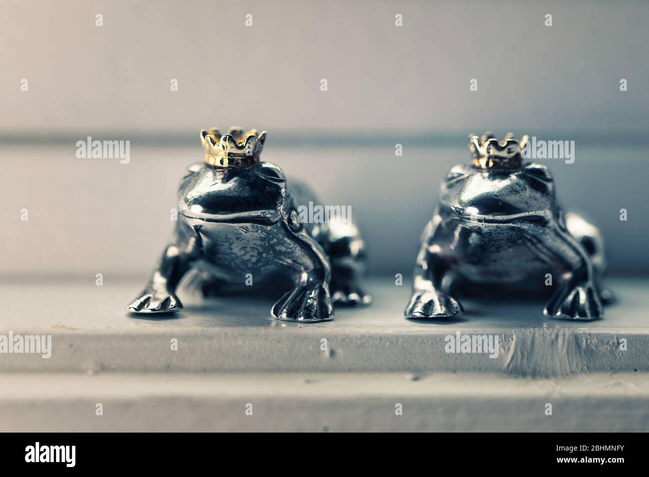 Deux figurines couronnées de prince grenouille en argent sterling assis dans le seuil de vent, concept de couleur. Banque D'Images