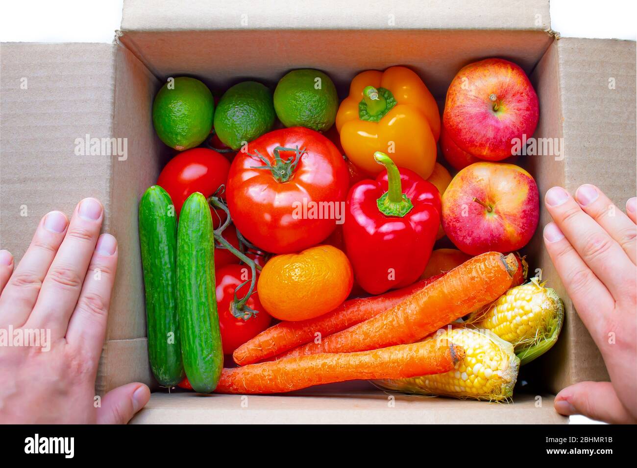 Une personne ouvrant une boîte de carton de livraison avec des produits, des fruits et des légumes à l'intérieur sur un fond blanc Banque D'Images