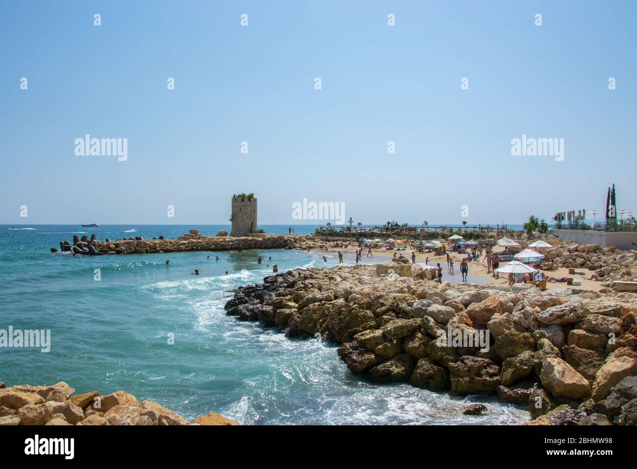 Seascape, vue sur une plage pleine de personnes, ancienne tour d'un château et rochers et tétrapodes, eau et ciel bleus, saison estivale, nature Banque D'Images