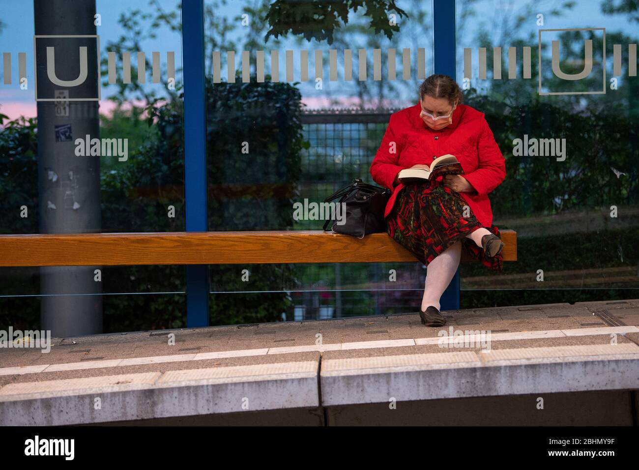 Stuttgart, Allemagne. 27 avril 2020. Une femme est assise avec un porte-parole auto-cousu à un arrêt des trams de Stuttgart (SSB) et lit un livre. Afin de ralentir la propagation du virus corona, la plupart des États allemands rendent désormais obligatoires les masques dans les transports publics et lors des achats. Crédit: Sebastian Gollnow/dpa/Alay Live News Banque D'Images