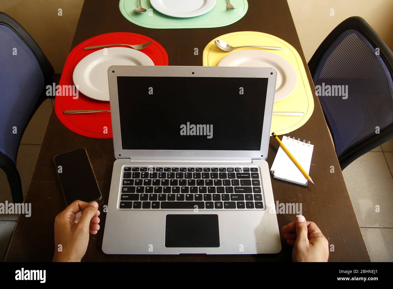 Photo d'ordinateur portable avec saisie des mains dessus, smartphone, ordinateur portable, crayon, assiettes et ustensiles sur une table à manger. Banque D'Images