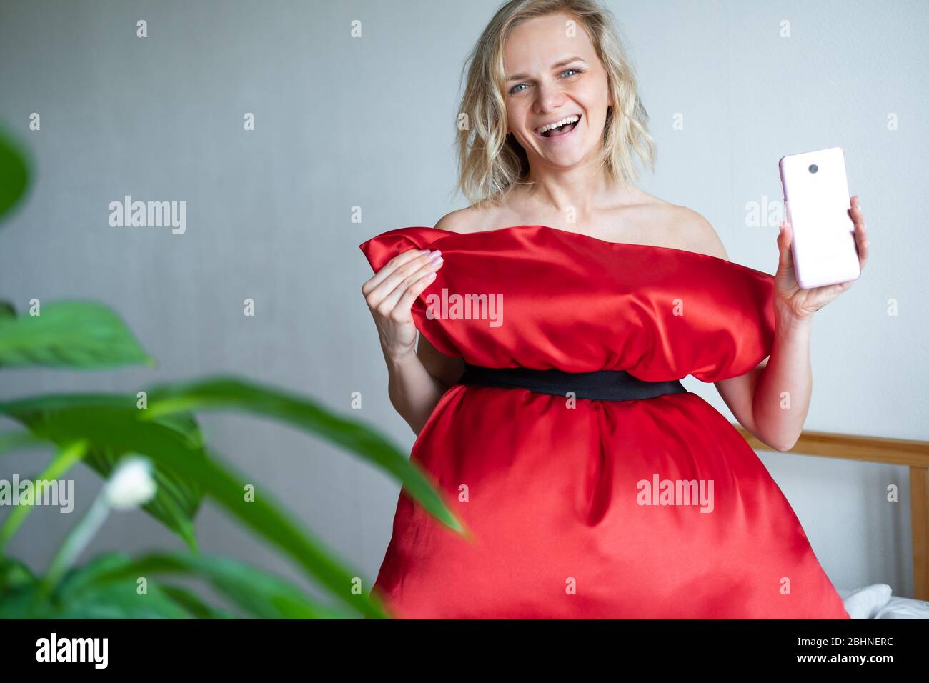 Une femme heureuse avec sa robe à oreiller rouge, qui fait de la photo selfie sur un téléphone portable pour un défi Crazy Pillow, en raison de son isolement à la maison. Quarantaine des caronavirus Banque D'Images