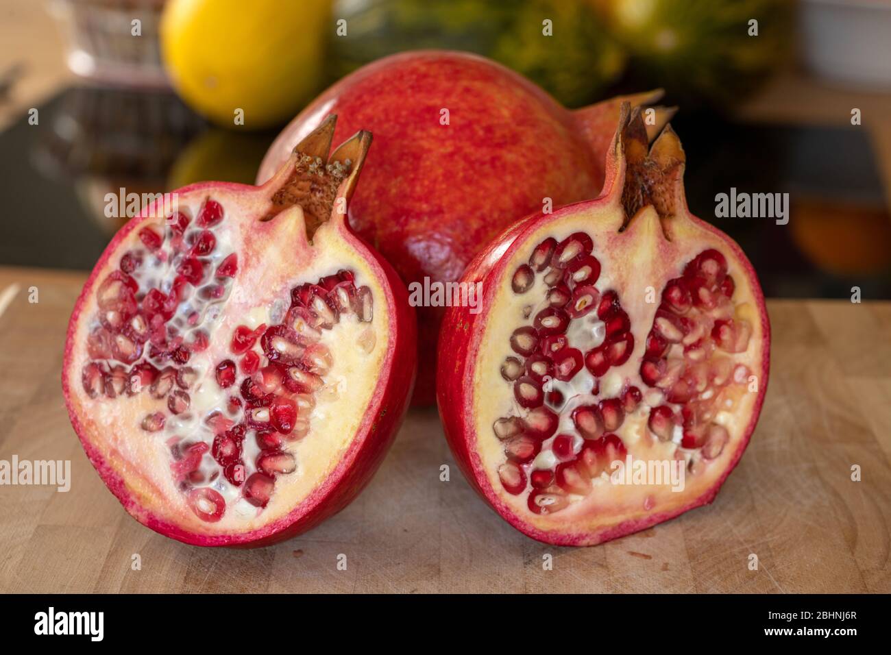 Gros plan sur un tout et deux demi-grenades de fruits sur une planche à découper en bois dans une cuisine domestique Banque D'Images
