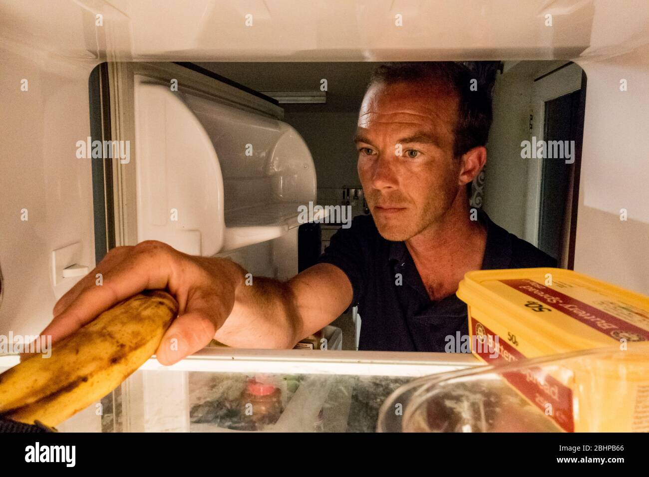 LEOMINSTER, ROYAUME-UNI - 25 AVRIL 2020: Un homme arrive dans son réfrigérateur pour une banane comme collation de nuit à 3 heures du matin à Leominster, Herefordshire sur UN Banque D'Images
