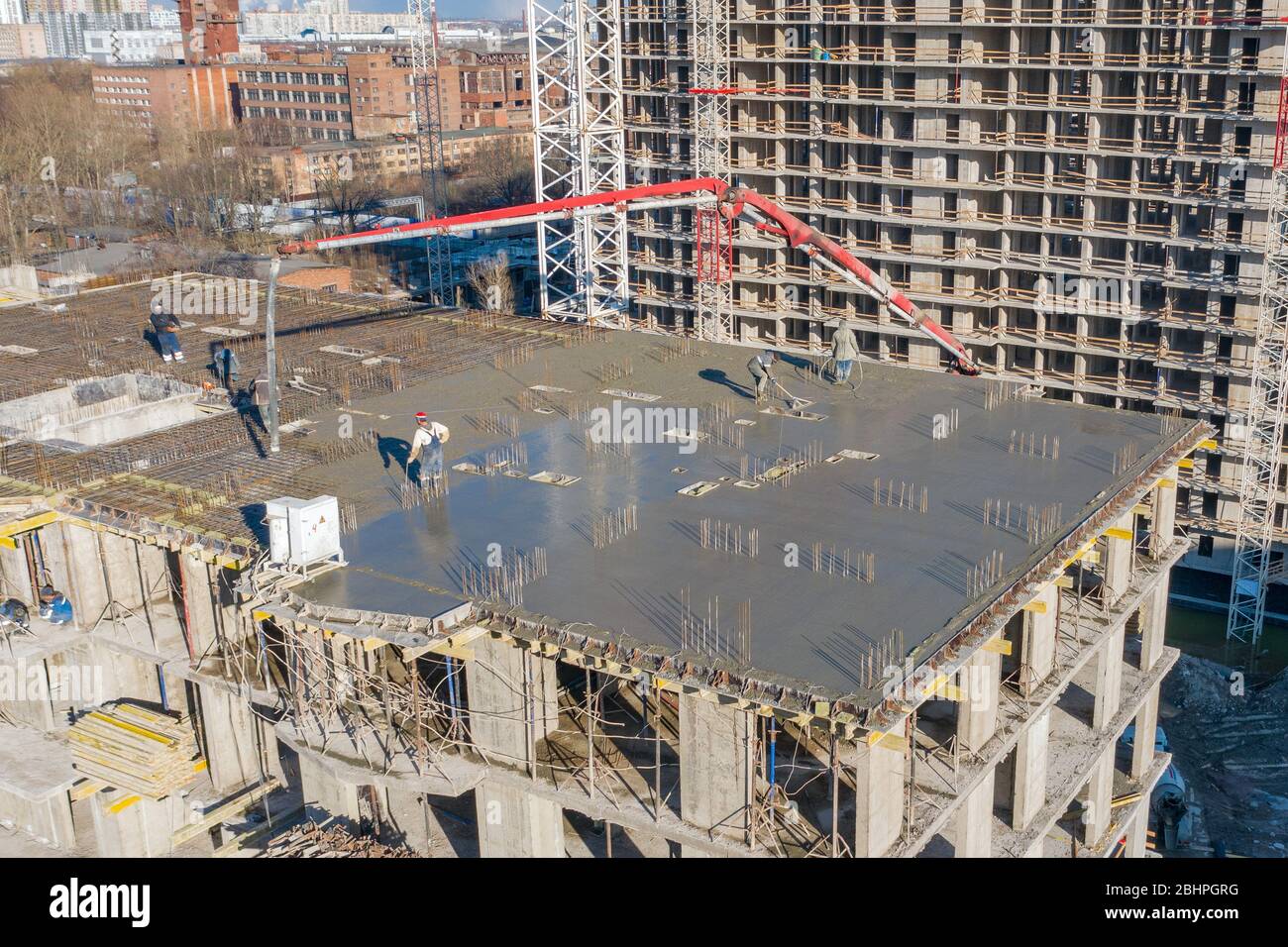 Verser du ciment sur les sols d'un bâtiment résidentiel à plusieurs étages en construction à l'aide d'un camion à pompe en béton à forte flèche pour alimenter le mélange t Banque D'Images