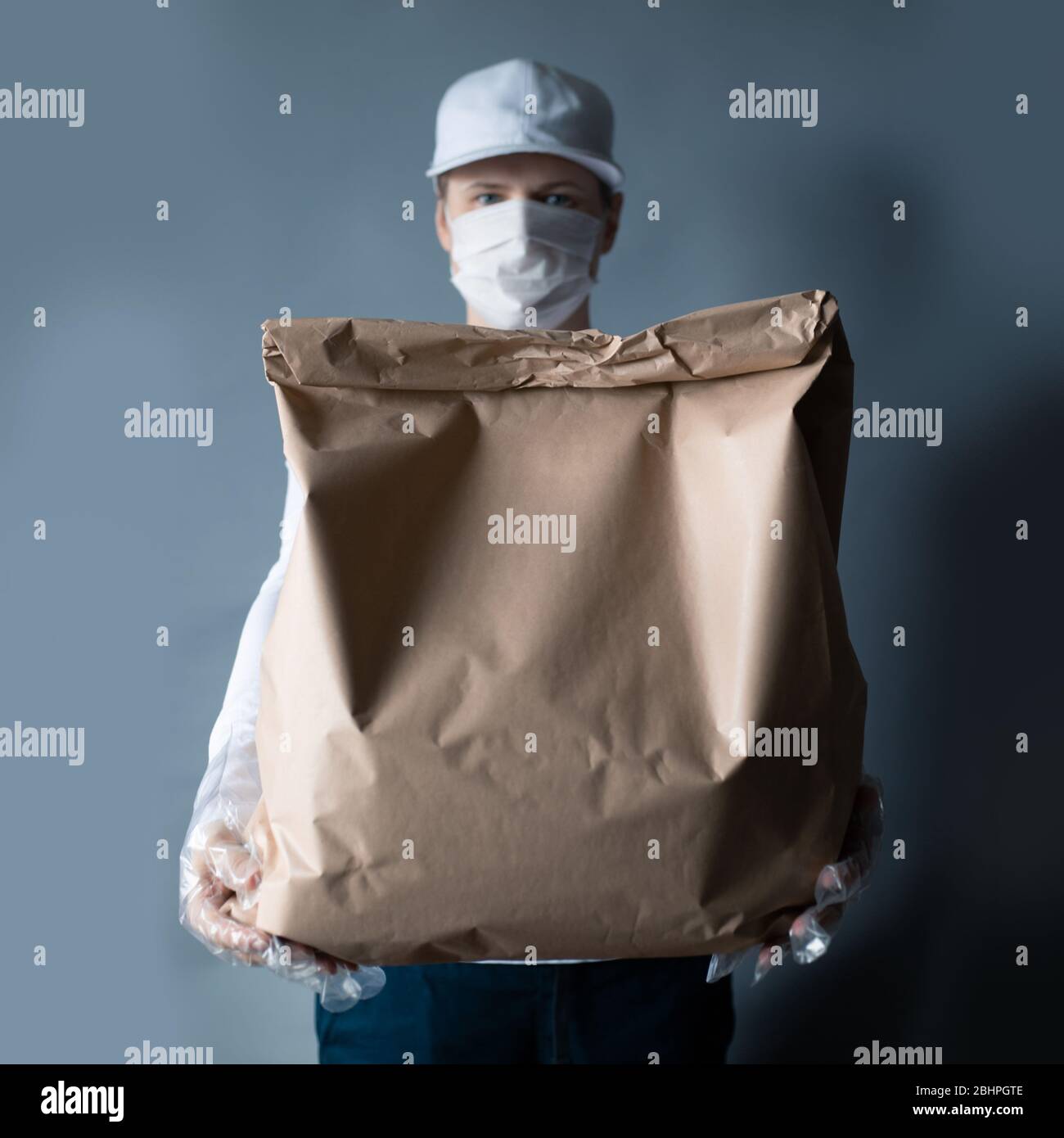 Livraison sûre de nourriture ou de marchandises. Un jeune courrier livrant une commande de sacs en papier brun ECO à la maison du client avec masque et gants pendant la couronne Banque D'Images