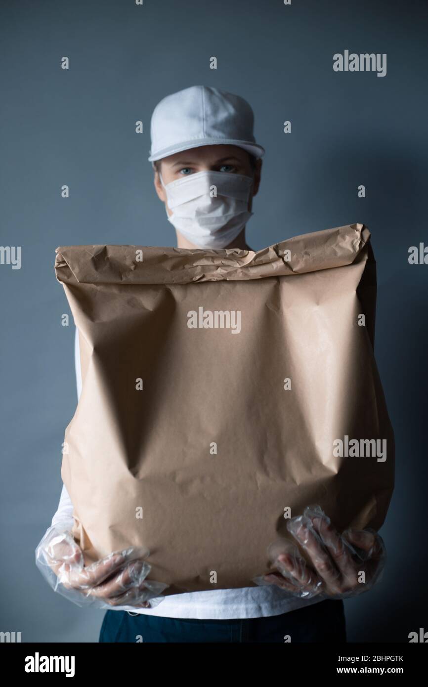 Livraison sûre de nourriture ou de marchandises. Un jeune courrier livrant une commande de sacs en papier brun ECO à la maison du client avec masque et gants pendant la couronne Banque D'Images