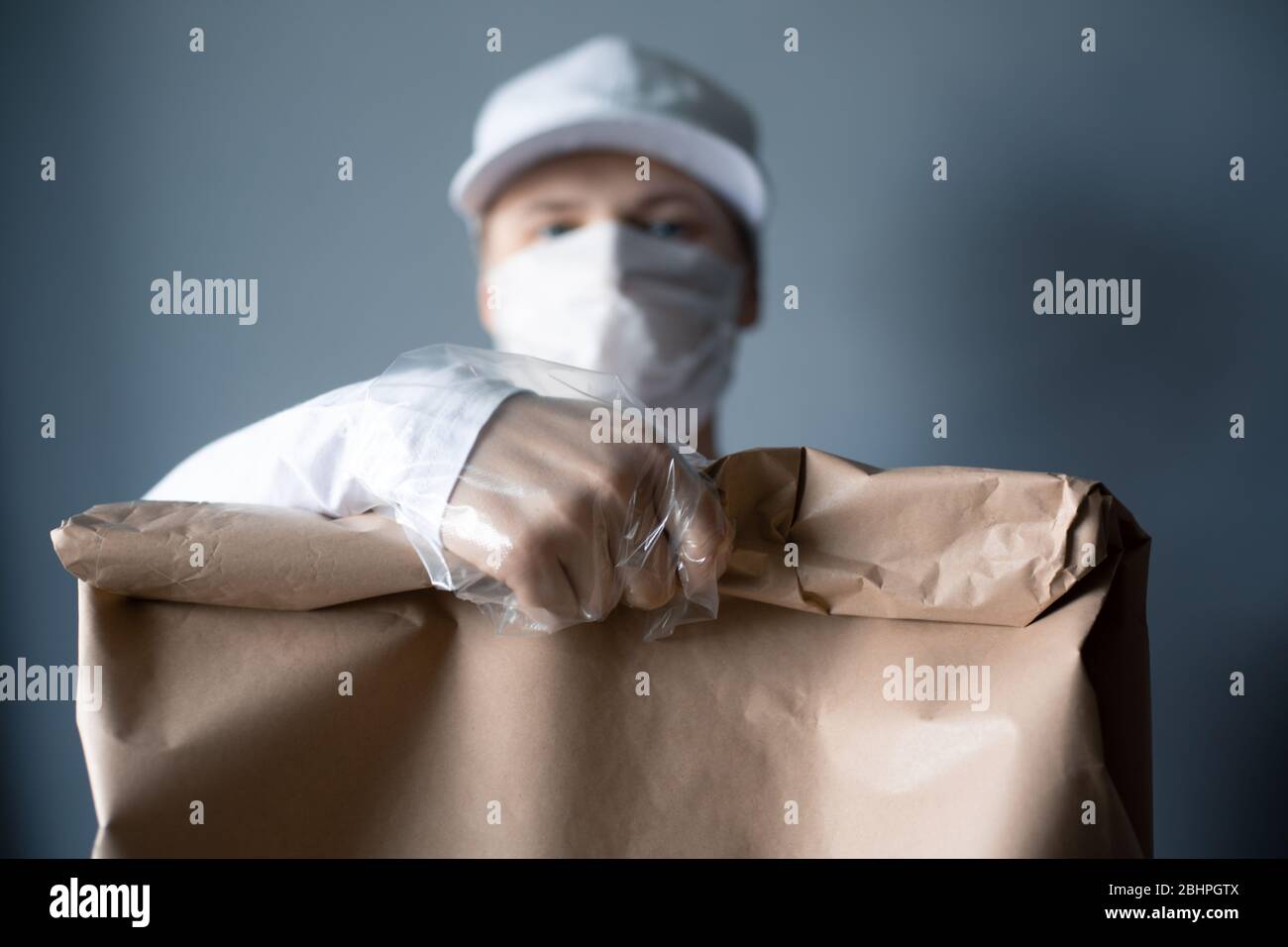 Livraison sûre de nourriture ou de marchandises. Un jeune courrier livrant une commande de sacs en papier brun ECO à la maison du client avec masque et gants pendant la couronne Banque D'Images