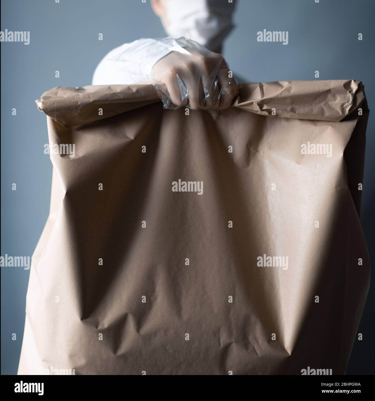 Livraison sûre de nourriture ou de marchandises. Un jeune courrier livrant une commande de sacs en papier brun ECO à la maison du client avec masque et gants pendant la couronne Banque D'Images