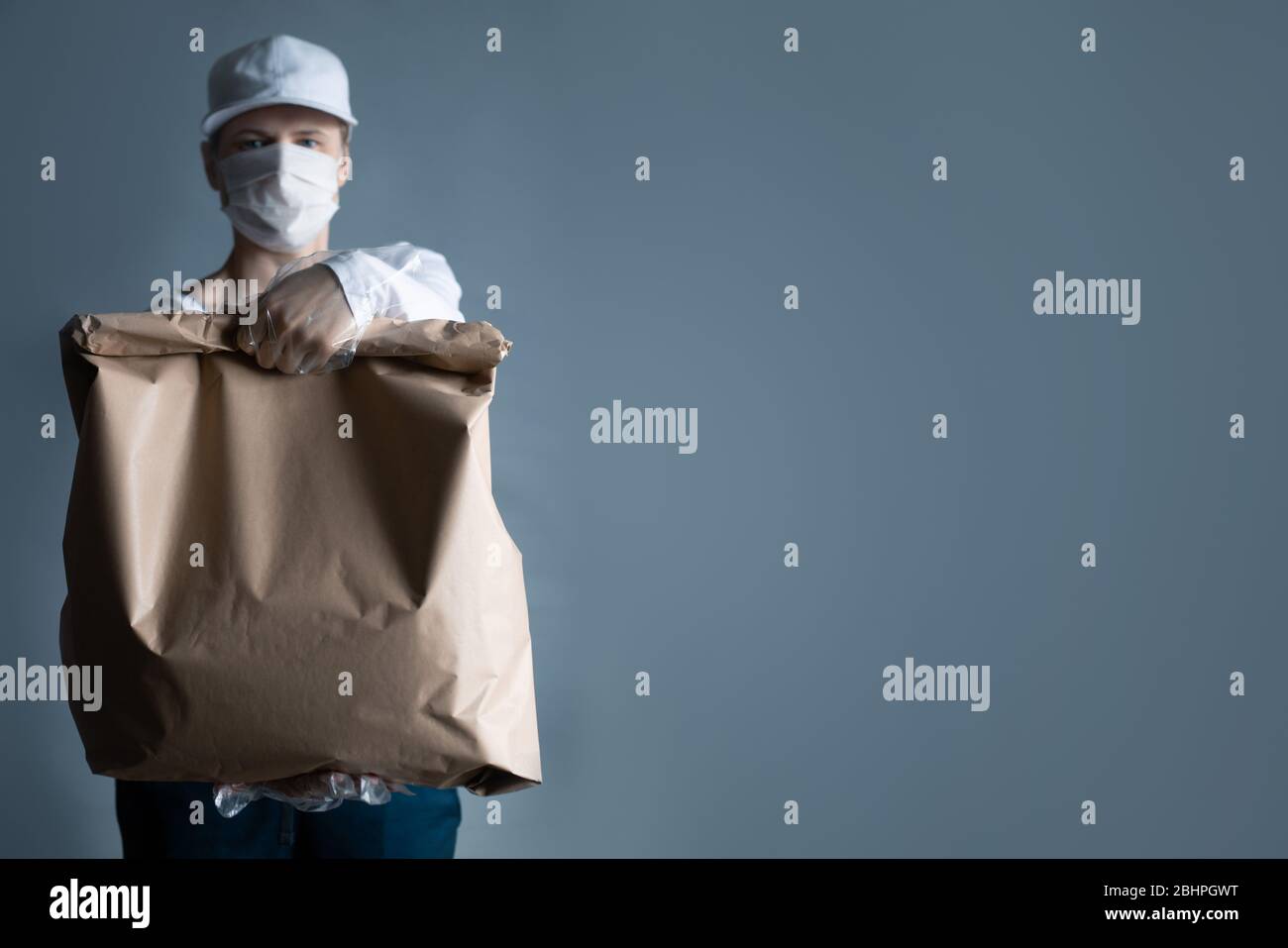 Livraison sûre de nourriture ou de marchandises. Un jeune courrier livrant une commande de sacs en papier brun ECO à la maison du client avec masque et gants pendant la couronne Banque D'Images