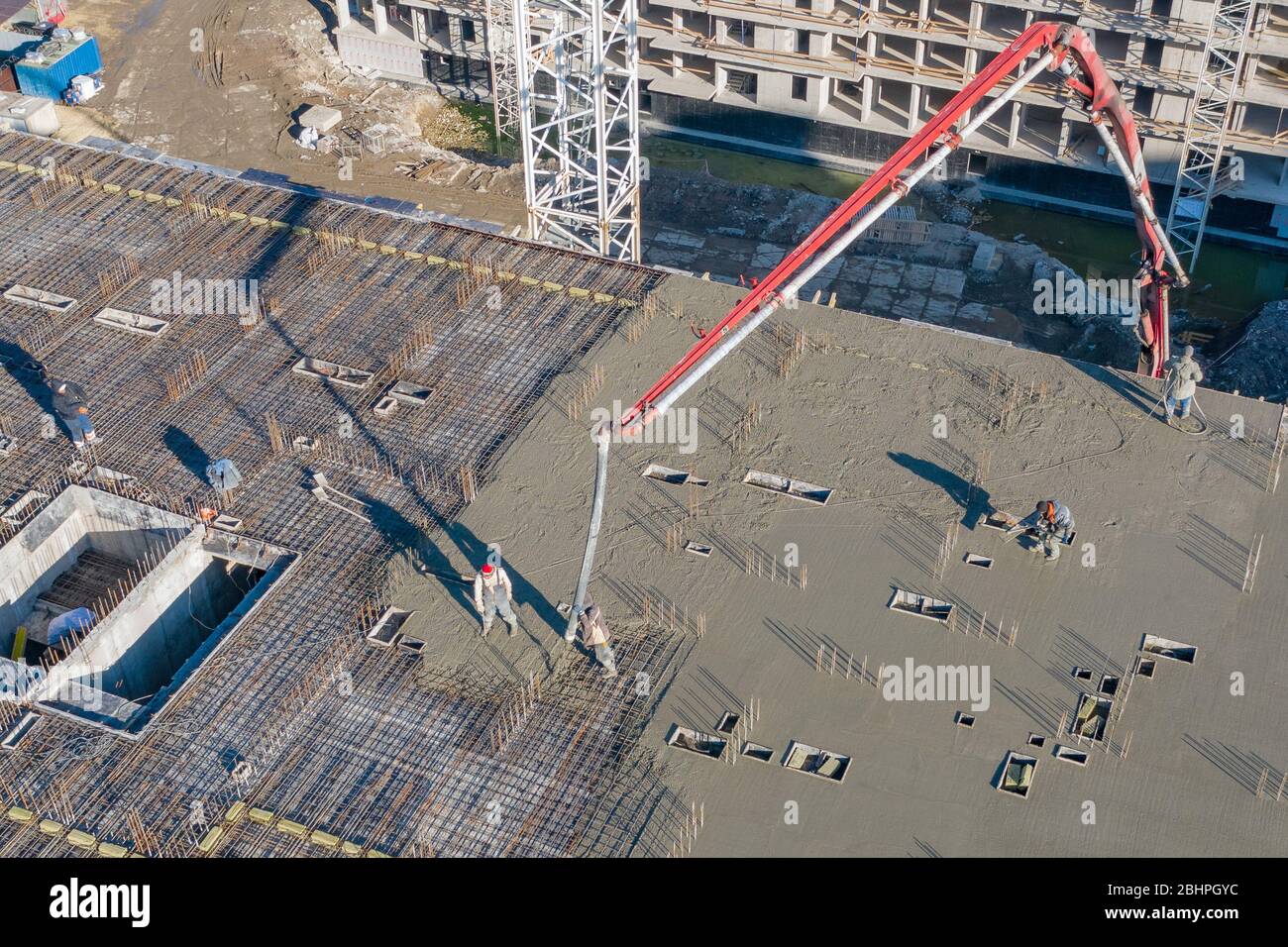 Verser du ciment sur les sols d'un bâtiment résidentiel à plusieurs étages en construction à l'aide d'un camion à pompe en béton à forte flèche pour alimenter le mélange t Banque D'Images