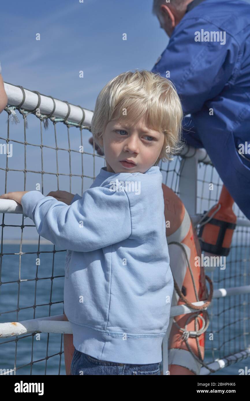 Blonde petit enfant accroché à la rampe sur le ferry, en regardant de retour pour jeter un coup d'oeil, en arrière-plan une belle mer bleue Banque D'Images