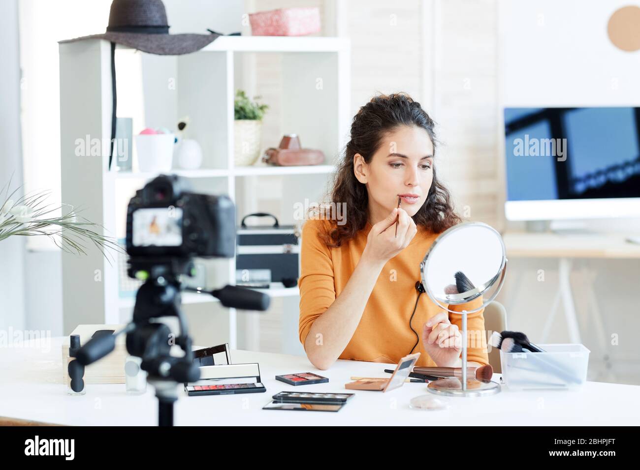 Blogueur de beauté assis à la table devant le miroir appliquant un crayon à lèvres sur l'appareil photo, prise horizontale Banque D'Images