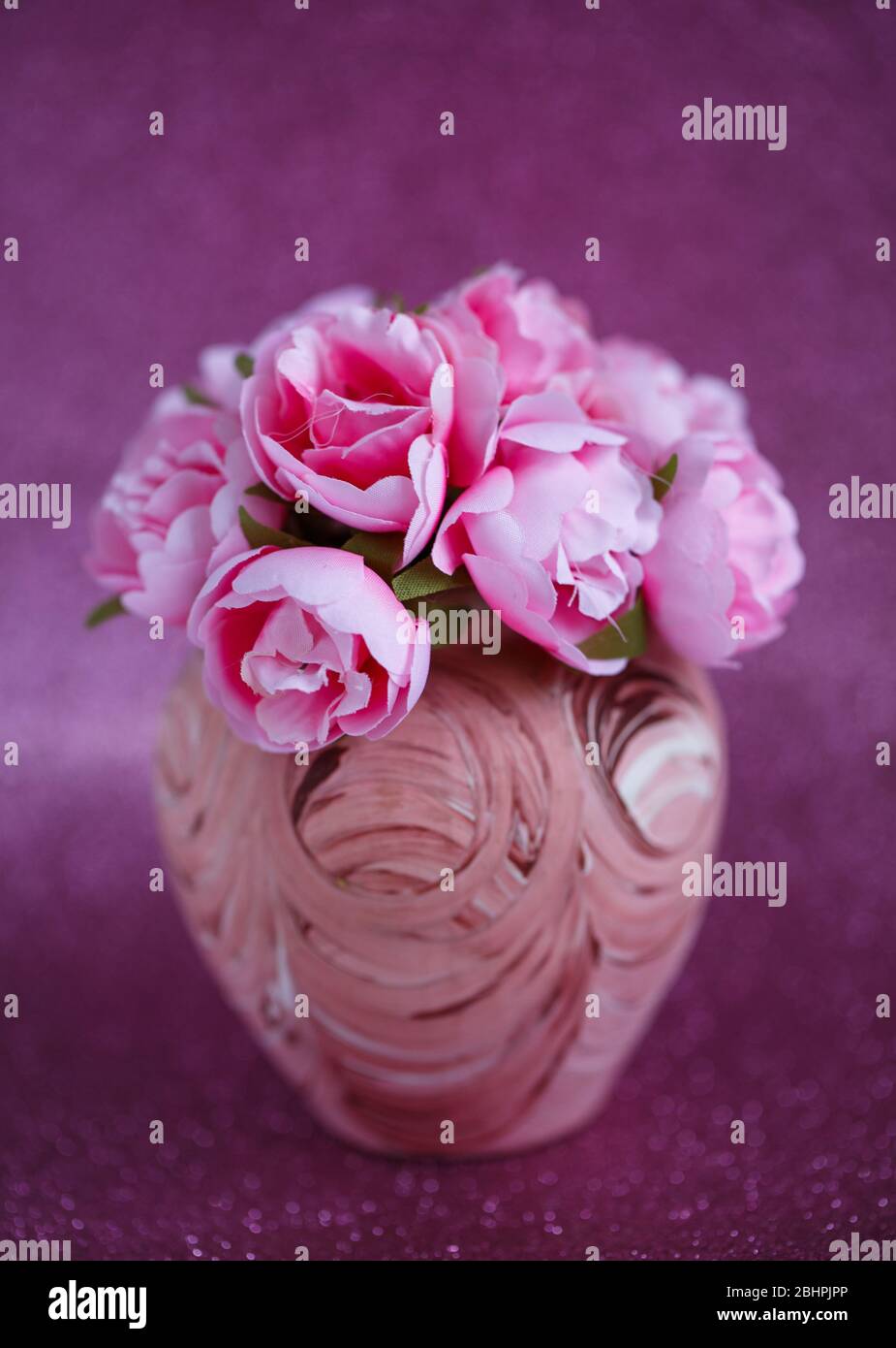 Belles petites fleurs roses dans un petit vase avec un motif sur un fond rose foncé brillant Banque D'Images