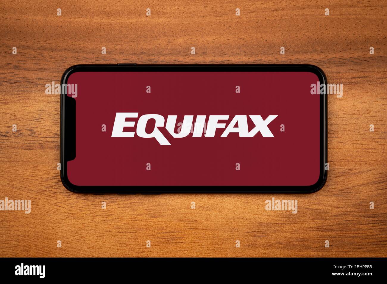 Un smartphone affichant le logo Equifax repose sur une table en bois ordinaire (usage éditorial uniquement). Banque D'Images