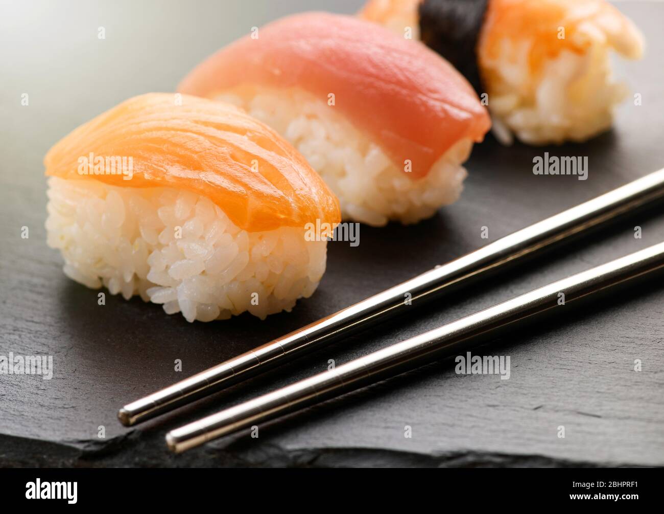 Gros plan sur une portion de sushi nighiri avec des tranches de saumon frais cru sur du riz salé pressé sur un plateau noir avec des baguettes Banque D'Images