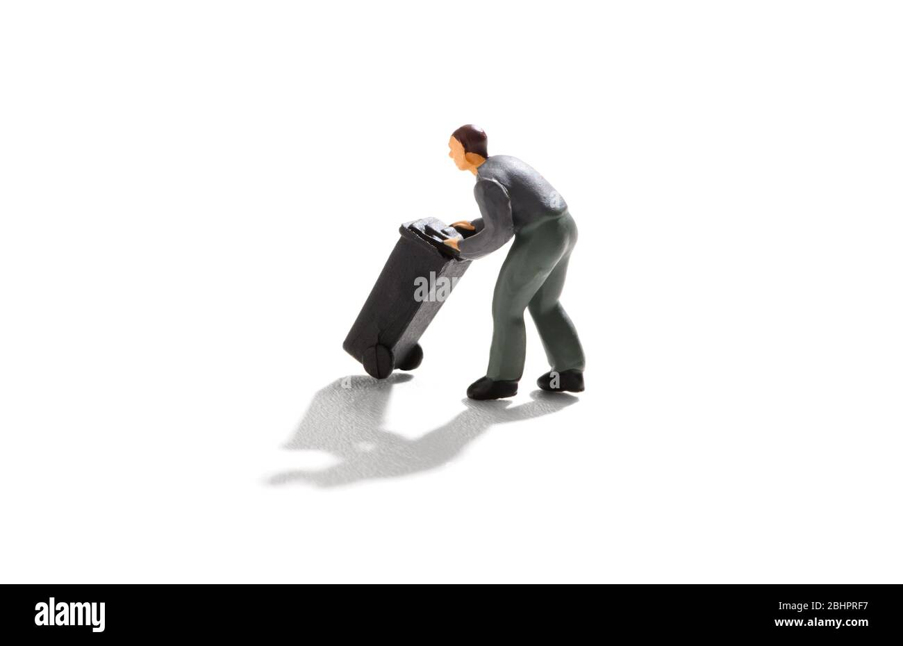 Homme miniature poussant une poubelle ou une roue noire sur un fond blanc avec ombre portée dans un concept d'élimination des déchets Banque D'Images