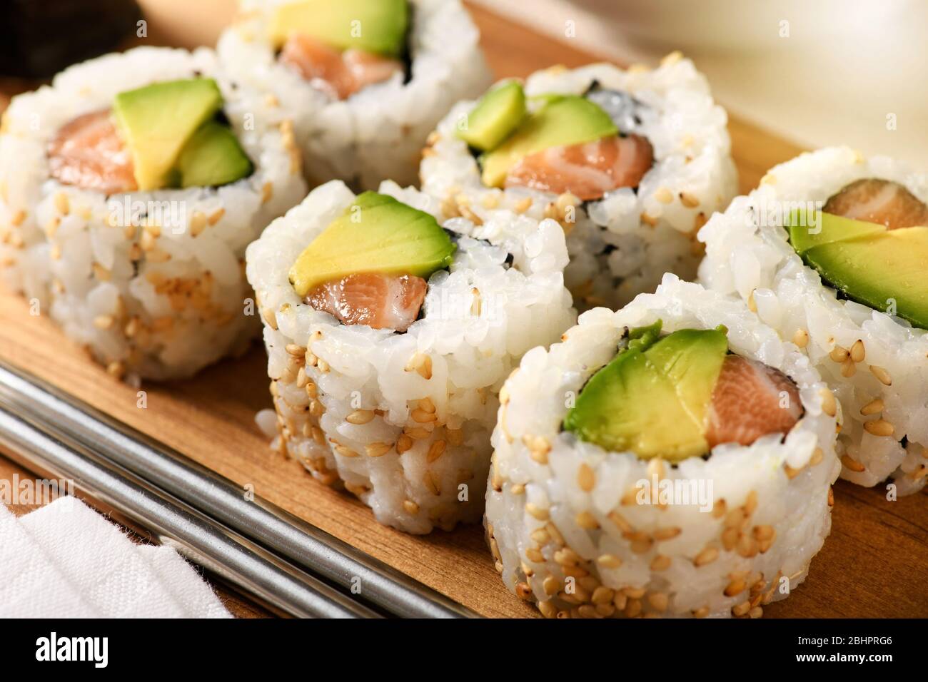 Les sushis uramaki de saumon traditionnel et d'avocat de poire roulés dans des graines de sésame et servis sur un plateau en bois en gros plan pour la publicité de menu Banque D'Images