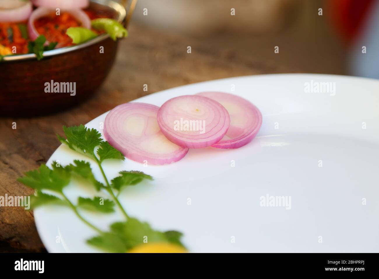 UNE ASSIETTE DE SALADE AVEC TRANCHES D'OIGNON, FEUILLES DE CITRON ET DE CORIANDRE DANS UNE PLAQUE EN CÉRAMIQUE BLANCHE. Banque D'Images