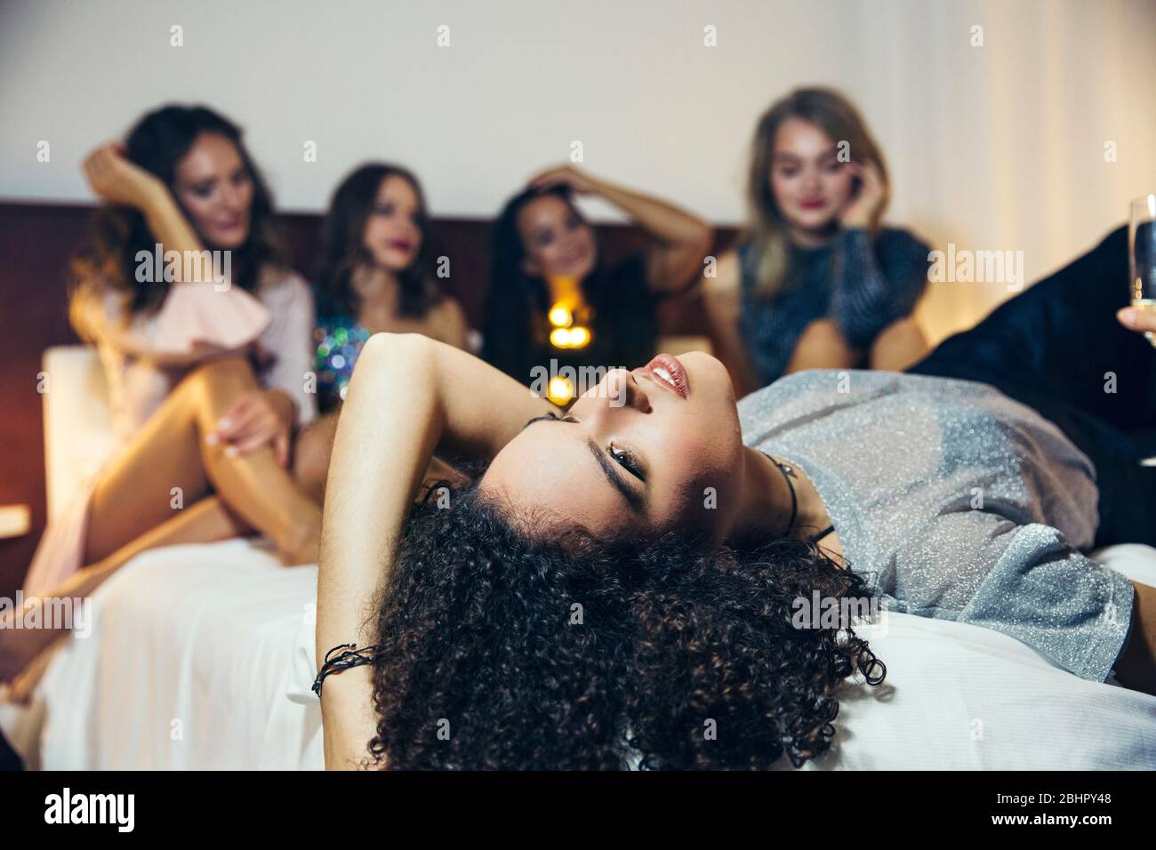 Cinq femmes habillées pour sortir pour la soirée assis et allongé sur un lit. Banque D'Images