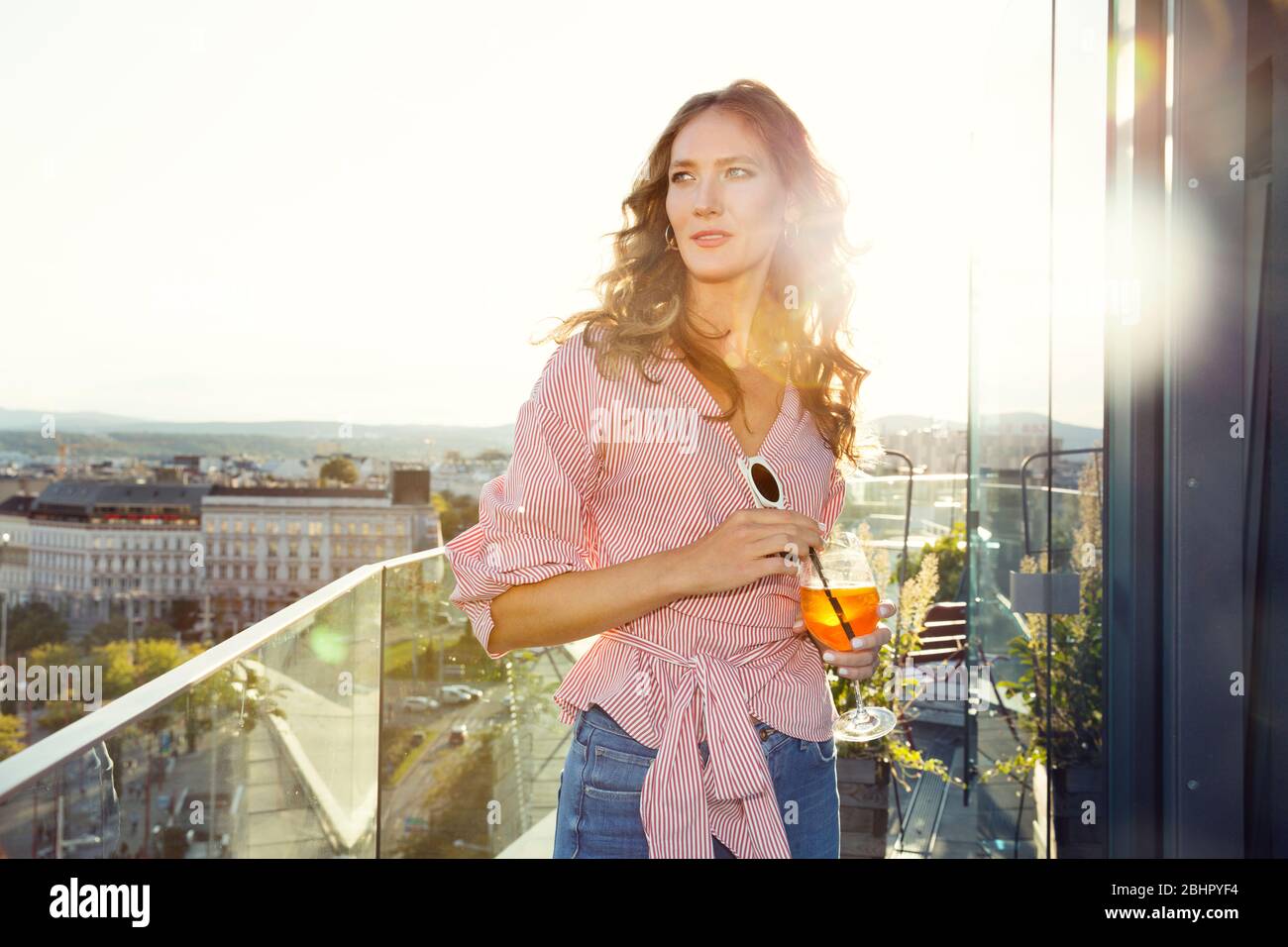 Une femme debout sur un balcon au soleil du soir avec une grande boisson Banque D'Images