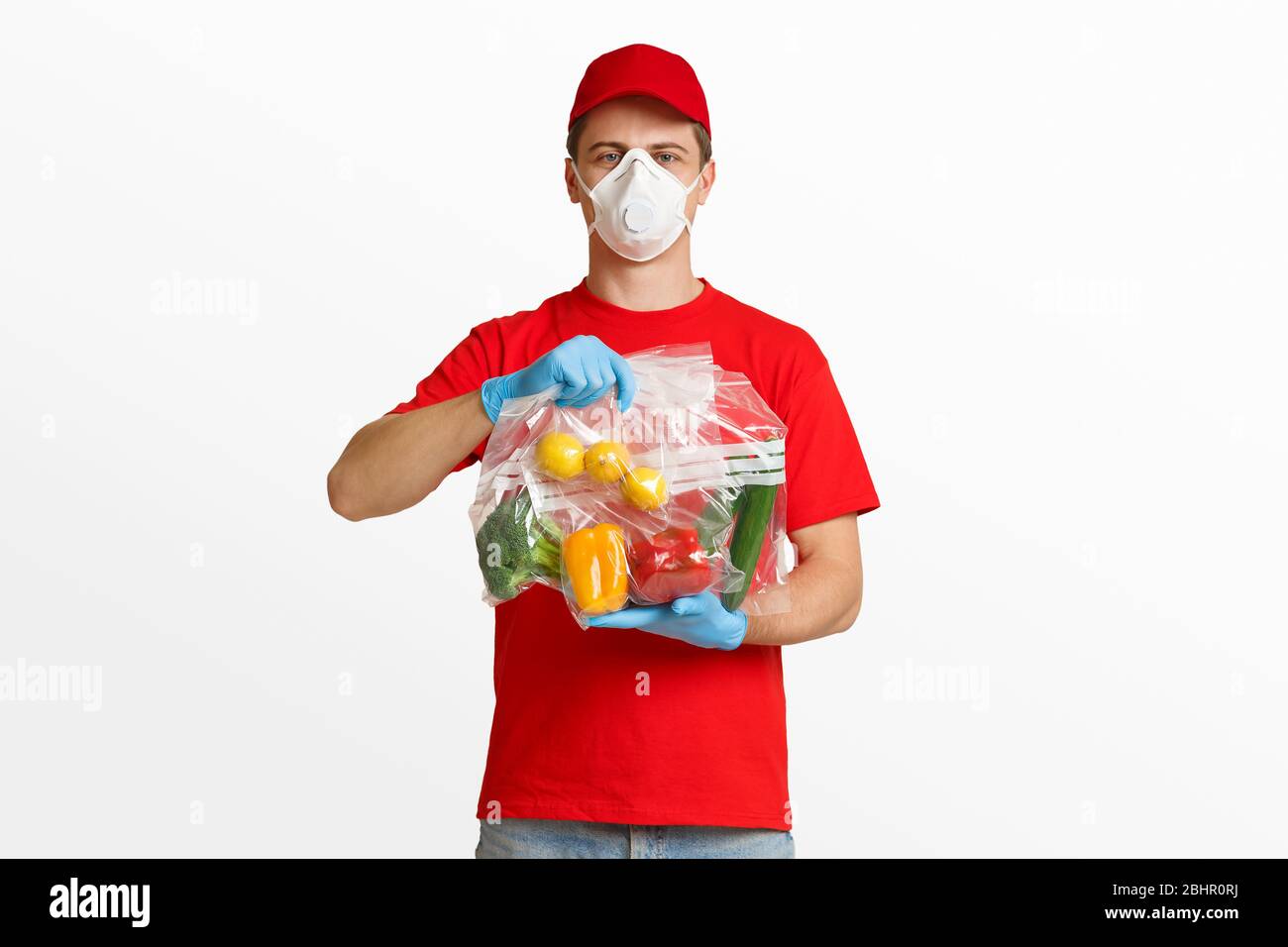 Légumes emballés dans des sacs dans les mains de l'homme de livraison dans le masque de protection Banque D'Images
