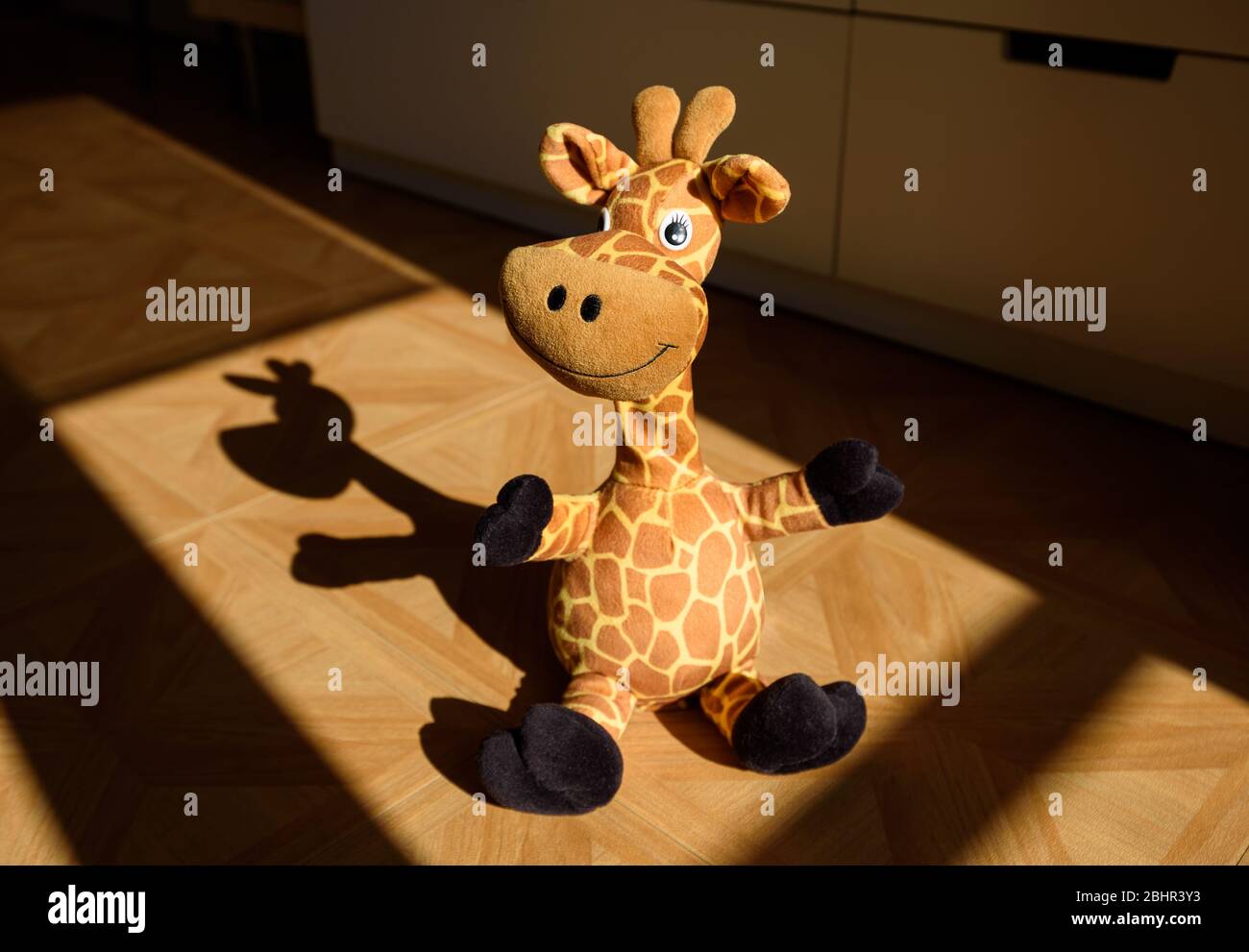 Mignonne girafe farcie dans la pièce d'un enfant illuminée par la lumière du soleil venant de la fenêtre et jetant une belle ombre sur le sol. Banque D'Images