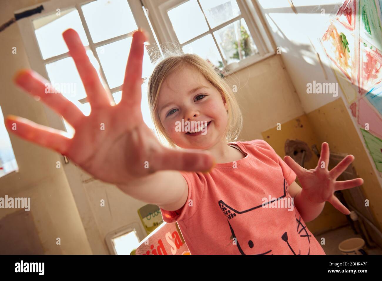 Sourire fille à l'intérieur pendant la crise du virus de Corona, faire la peinture de doigt, regarder l'appareil photo. Banque D'Images