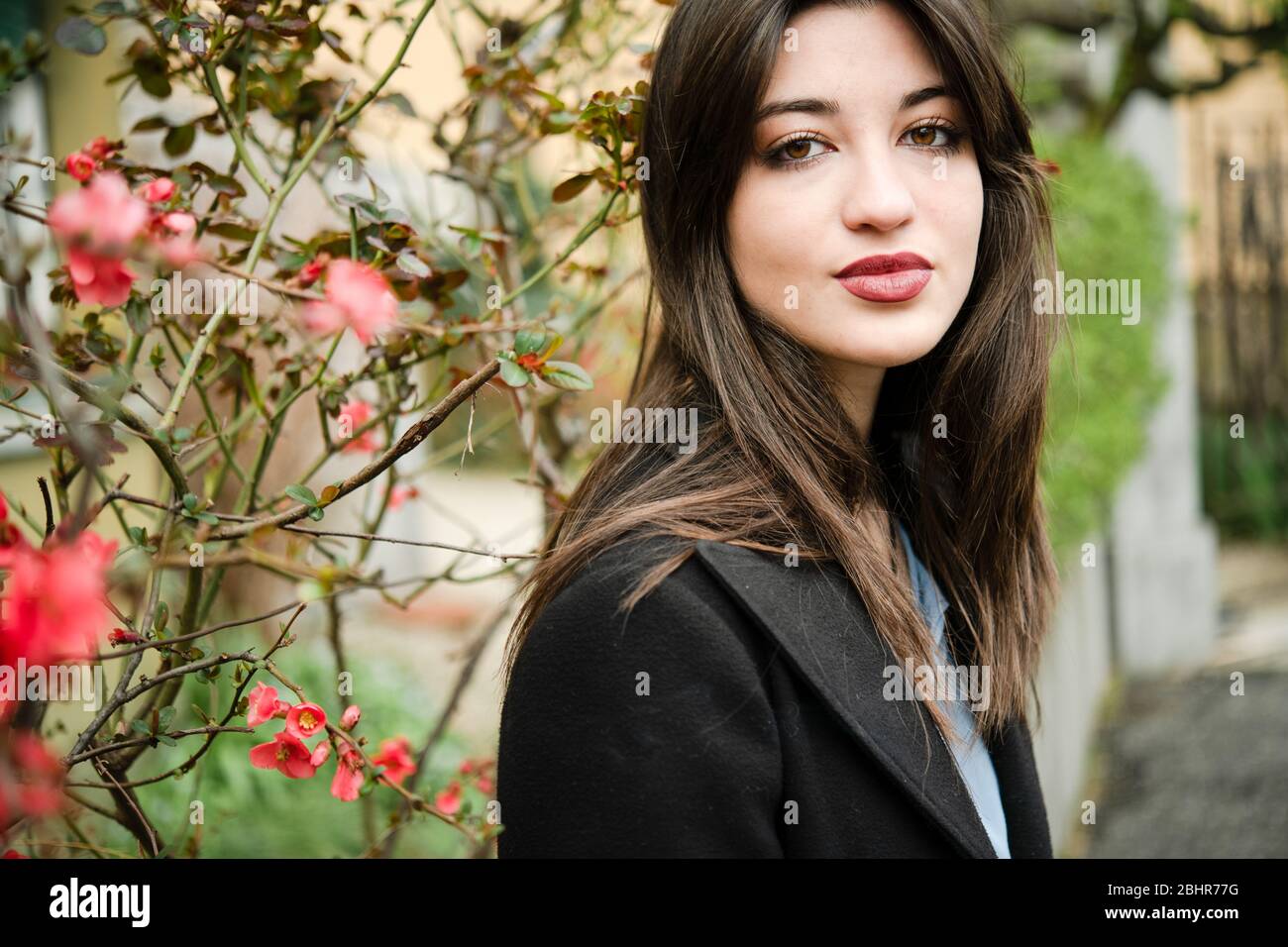Une femme avec de longs cheveux sombres debout dans le jardin nichent à un buisson avec des fleurs rouges. Banque D'Images