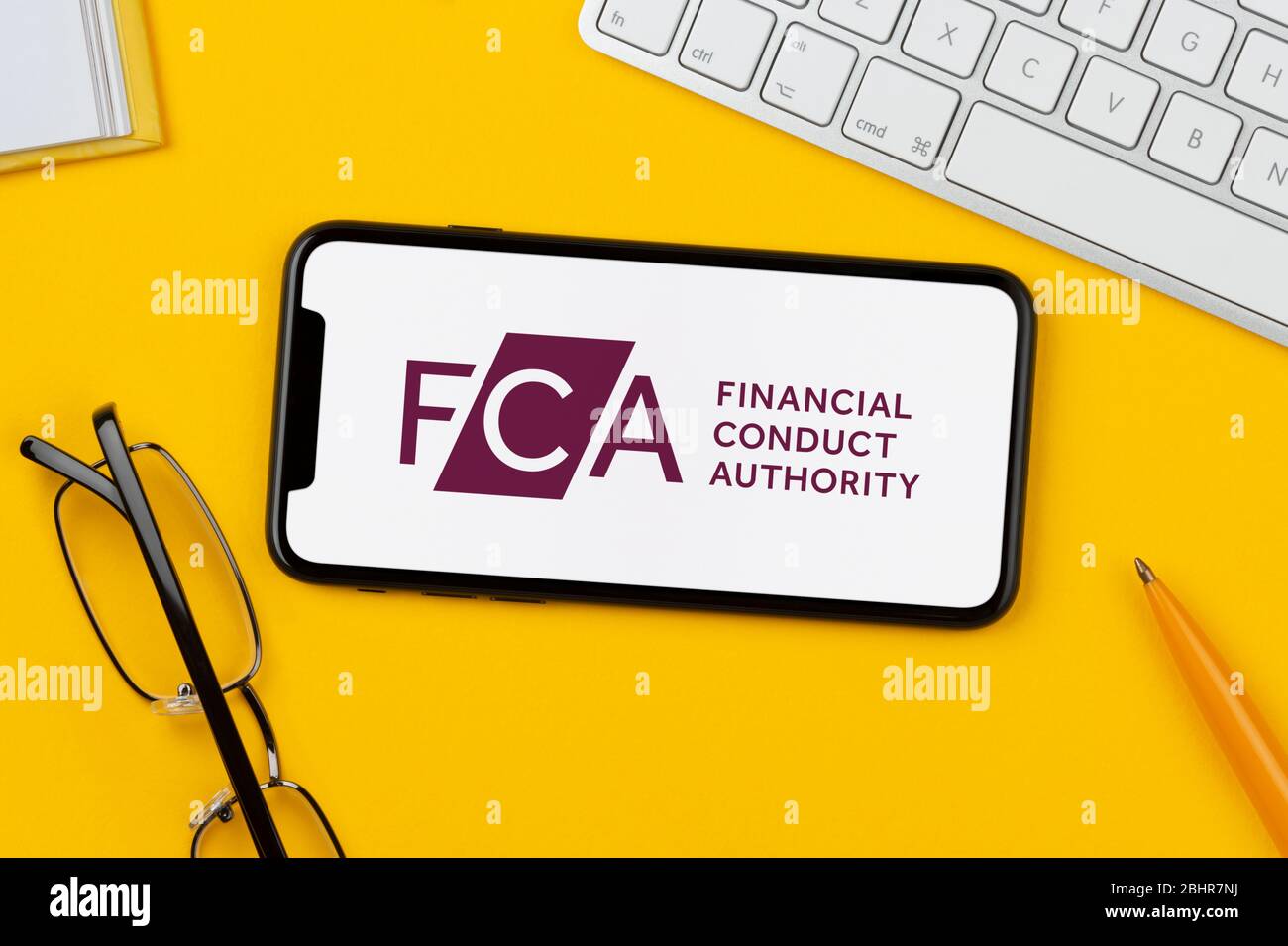Un smartphone affichant le logo FCA repose sur un fond jaune, ainsi qu'un clavier, des lunettes, un stylo et un livre (usage éditorial uniquement). Banque D'Images