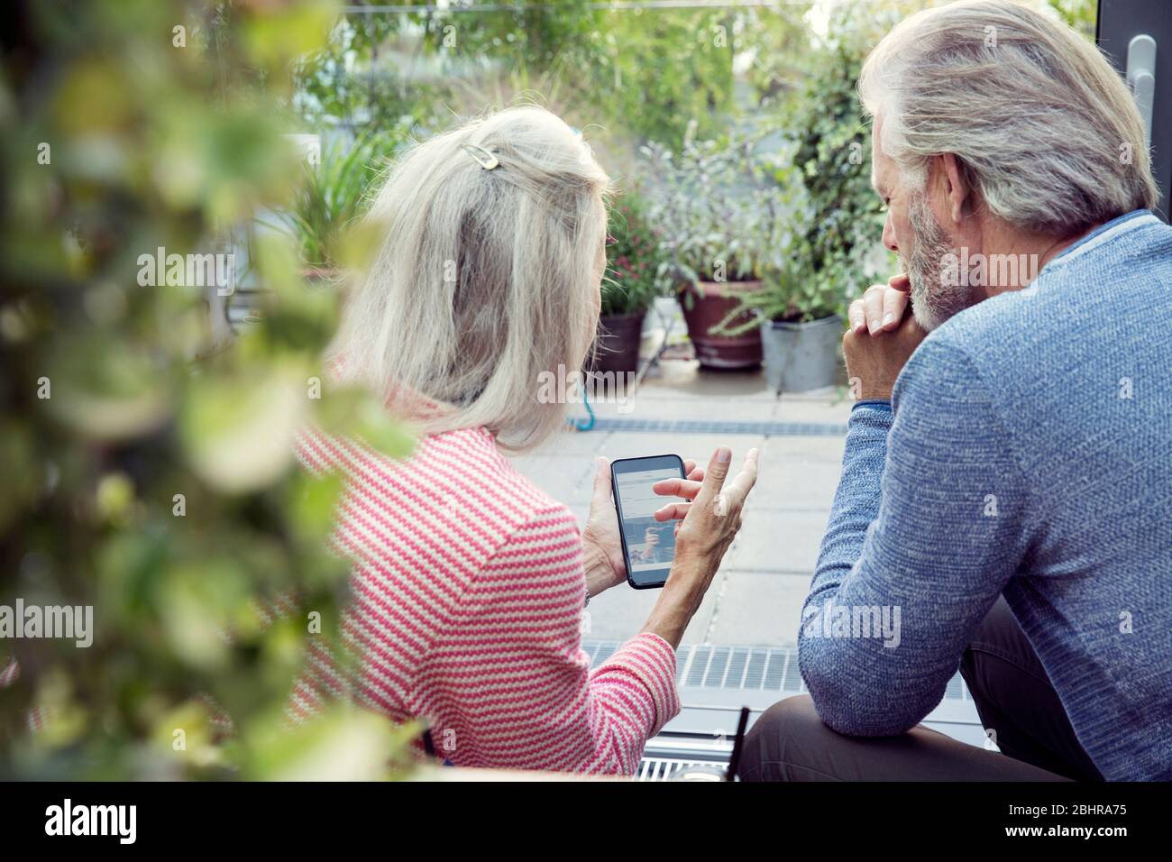 Vue arrière d'un couple assis dans un jardin et regardant un téléphone portable. Banque D'Images