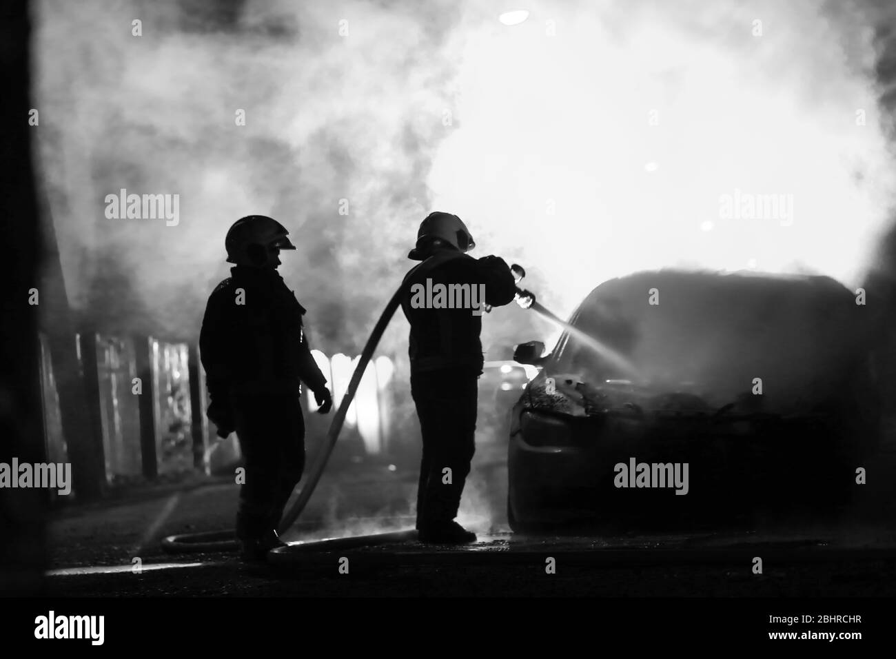 les pompiers qui combattent contre l'incendie à minuit. Voiture de police dans le dos. Noir et blanc Banque D'Images