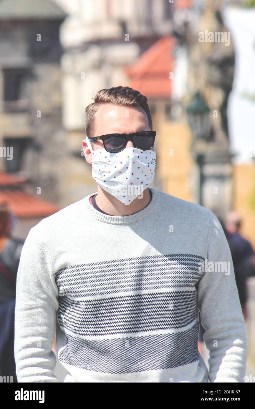 Jeune homme avec lunettes de soleil et masque en tissu cousu photographié sur le pont Charles à Prague, en République tchèque. Brouillé dans l'arrière-plan. Voyager, tourisme pendant coronavirus. COVID-19. Banque D'Images