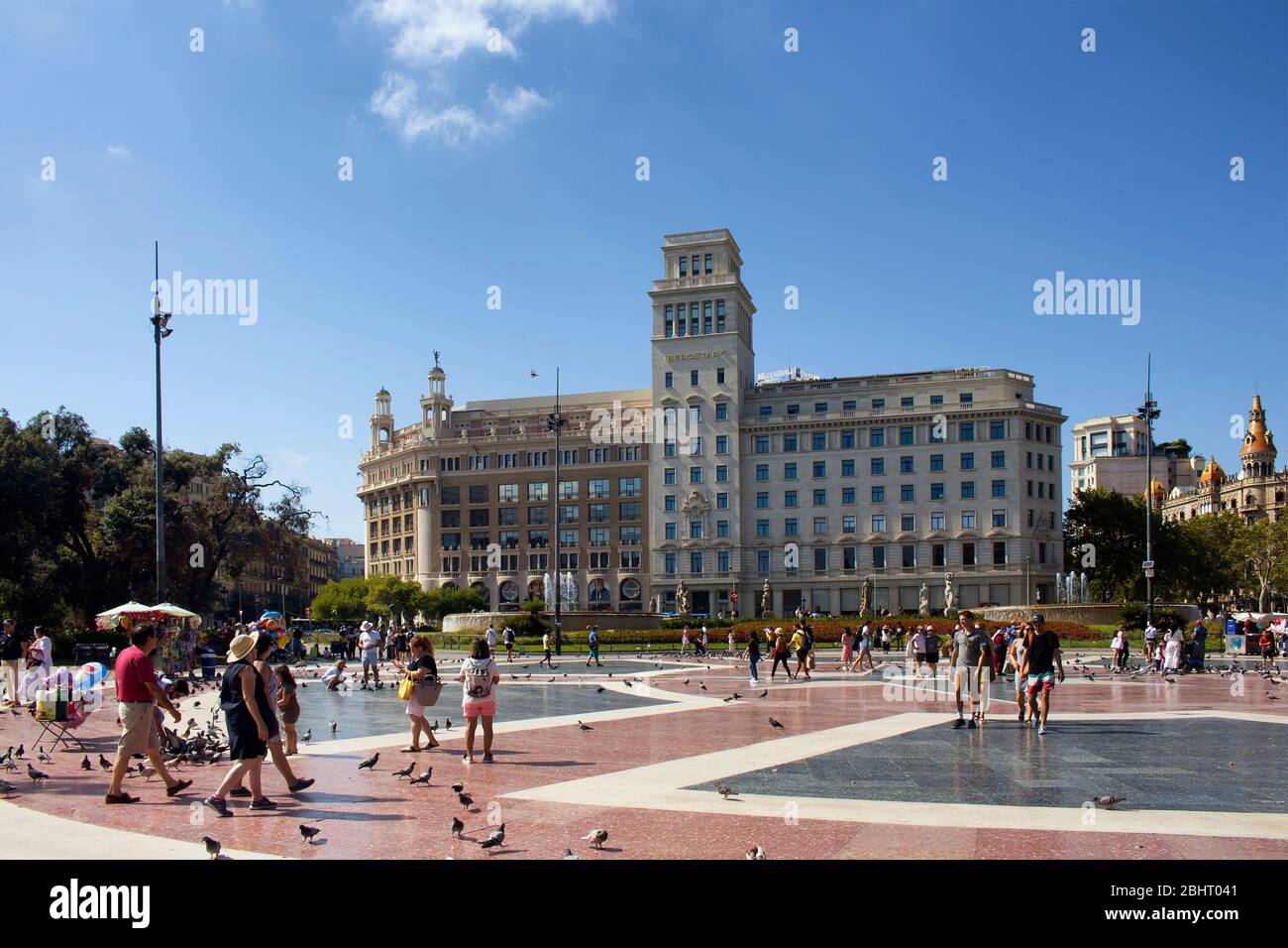 Vue sur les gens marchant sur la célèbre place de la ville appelée "Placa de Catalunya" à Barcelone. Le célèbre hôtel est en arrière-plan. C'est une journée d'été ensoleillée. Banque D'Images