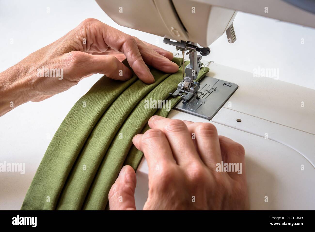 Vue rapprochée sur les mains d'une femme à l'aide d'une machine à coudre pour coudre des masques de visage en tissu de coton vert réutilisables faits maison. Banque D'Images