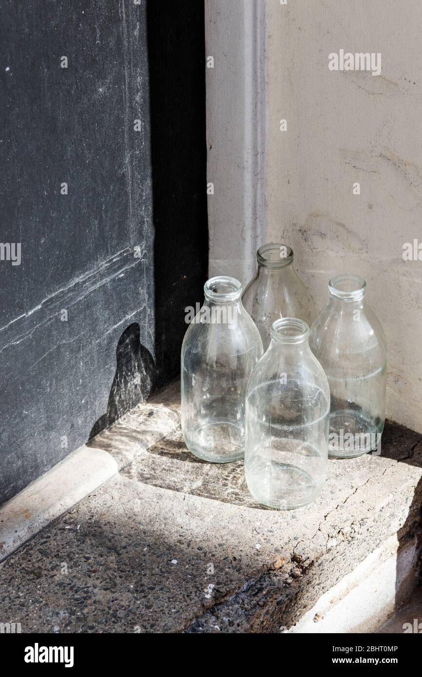 Quatre bouteilles de lait en verre vides en attente de collecte à la porte d'un établissement résidentiel Banque D'Images