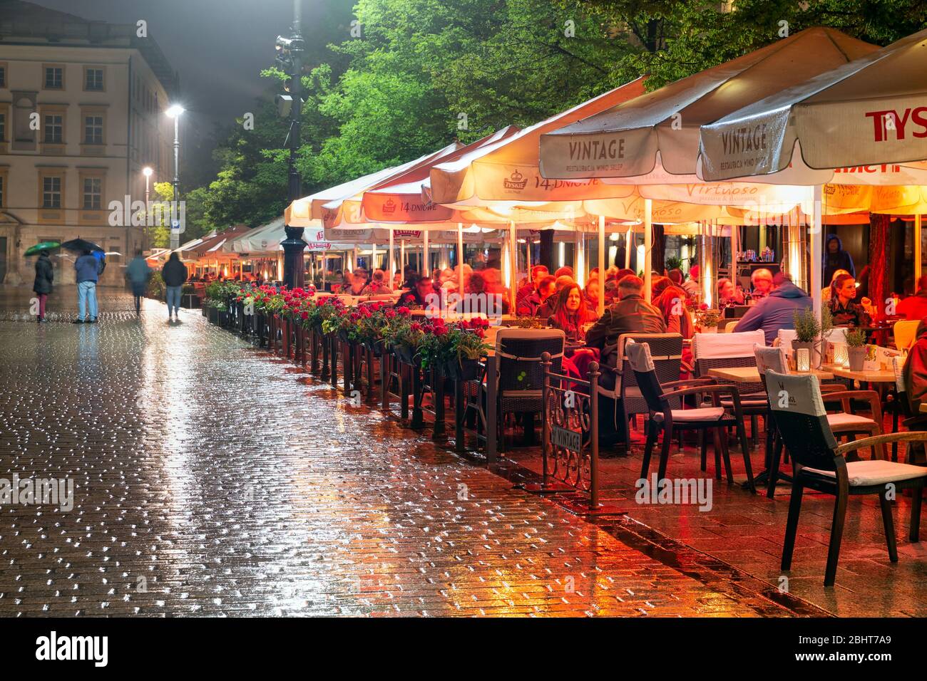 Soirée de pluie avec des personnes assises sur les terrasses de la place du marché de Cracovie Banque D'Images