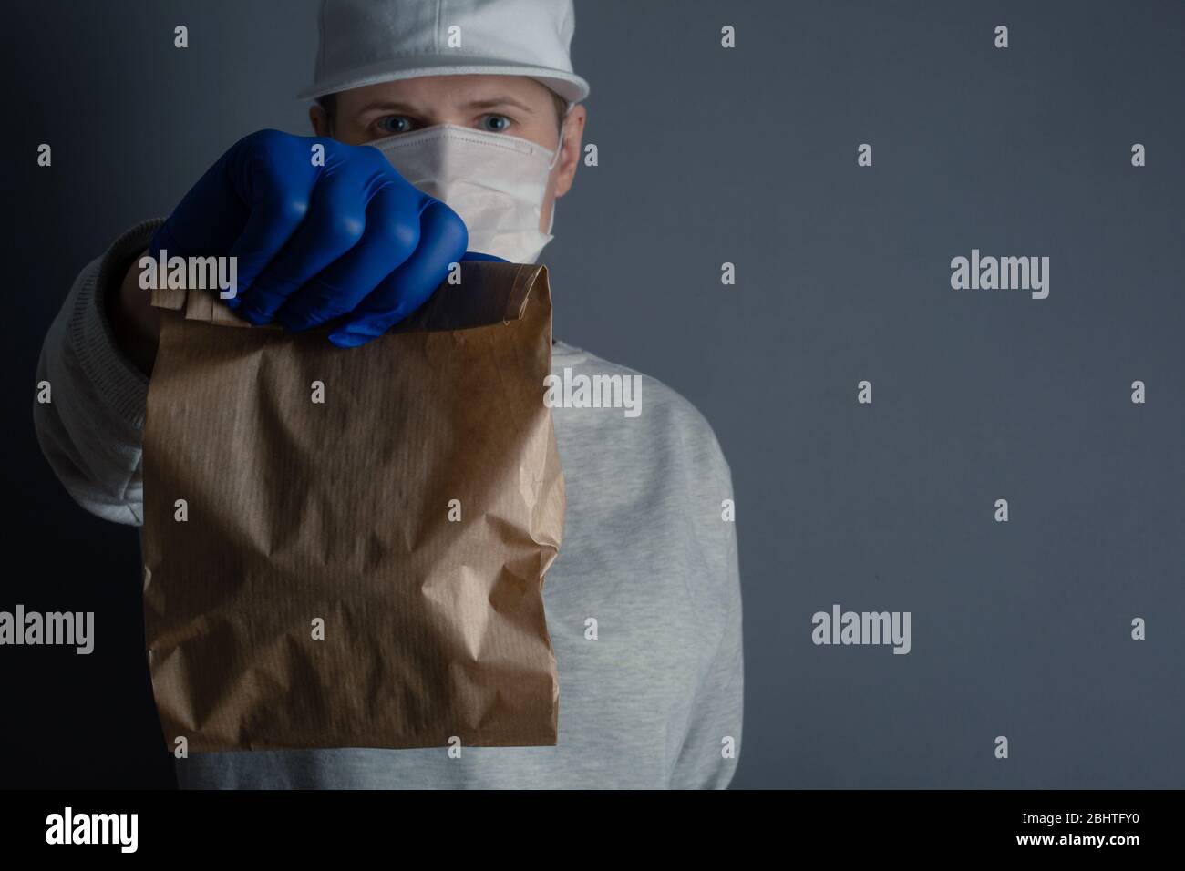 Livraison sûre de nourriture ou de marchandises. Un jeune courrier livrant une petite commande de sac en papier brun ECO à la maison du client avec masque et gants pendant le coronavi Banque D'Images